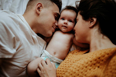Vater und Mutter liegen mit ihrem Baby in der Mitte